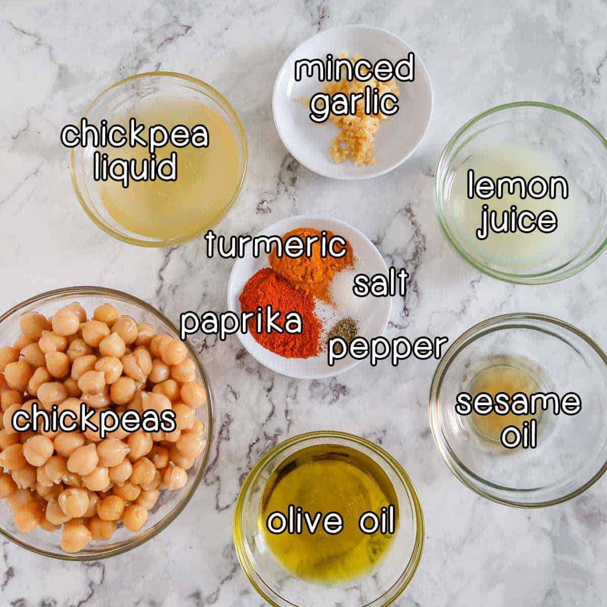 Overhead shot of ingredients- chickpeas, chickpea liquid, minced garlic, lemon juice, sesame oil, olive oil, paprika, turmeric, salt, and pepper.