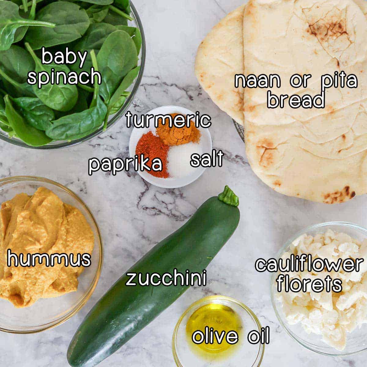 Overhead shot of ingredients- baby spinach, naan or pita bread, turmeric, paprika, salt, hummus, zucchini, olive oil, and cauliflower florets.