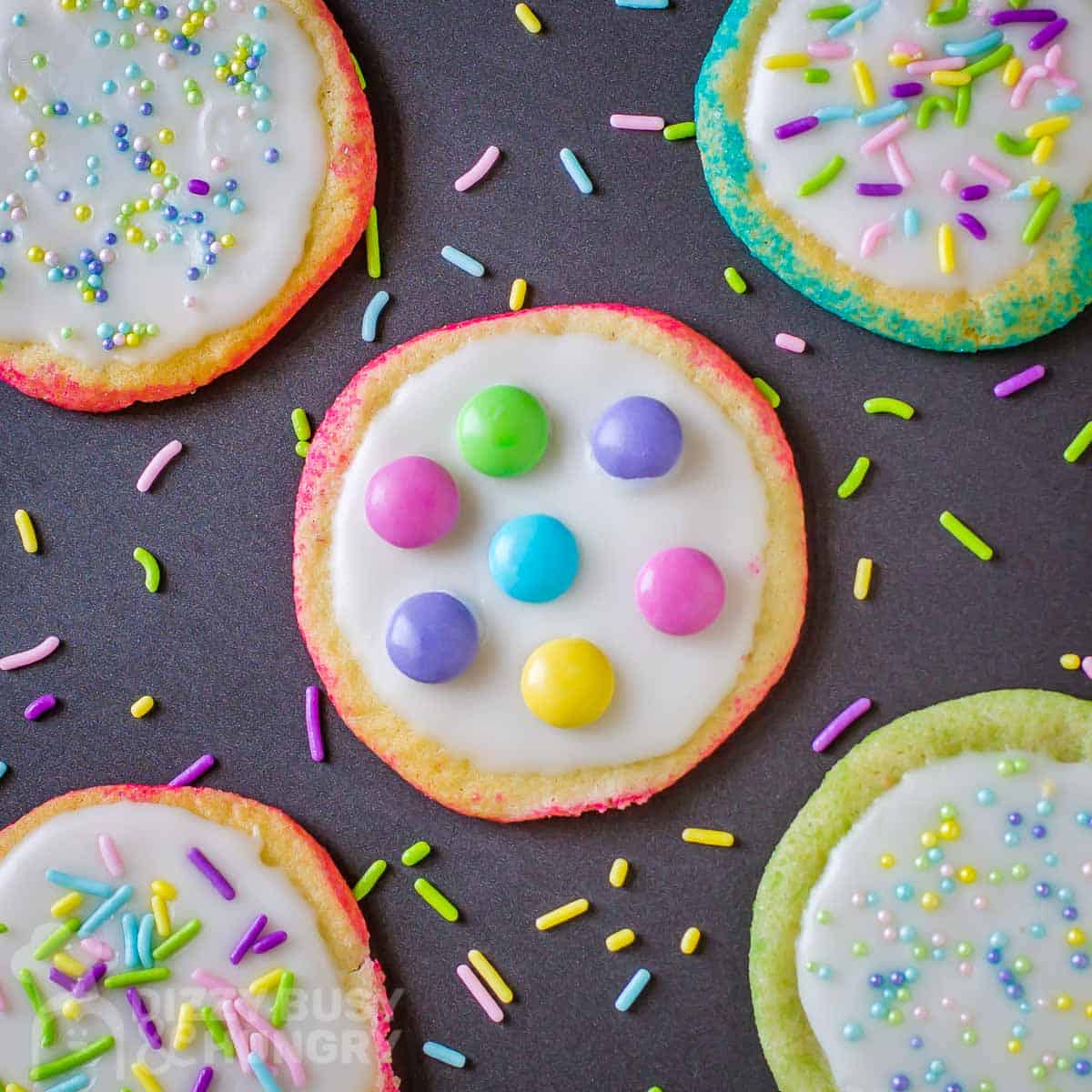 Overhead shot of easter sugar cookies with sprinkles and candies on a black surface.