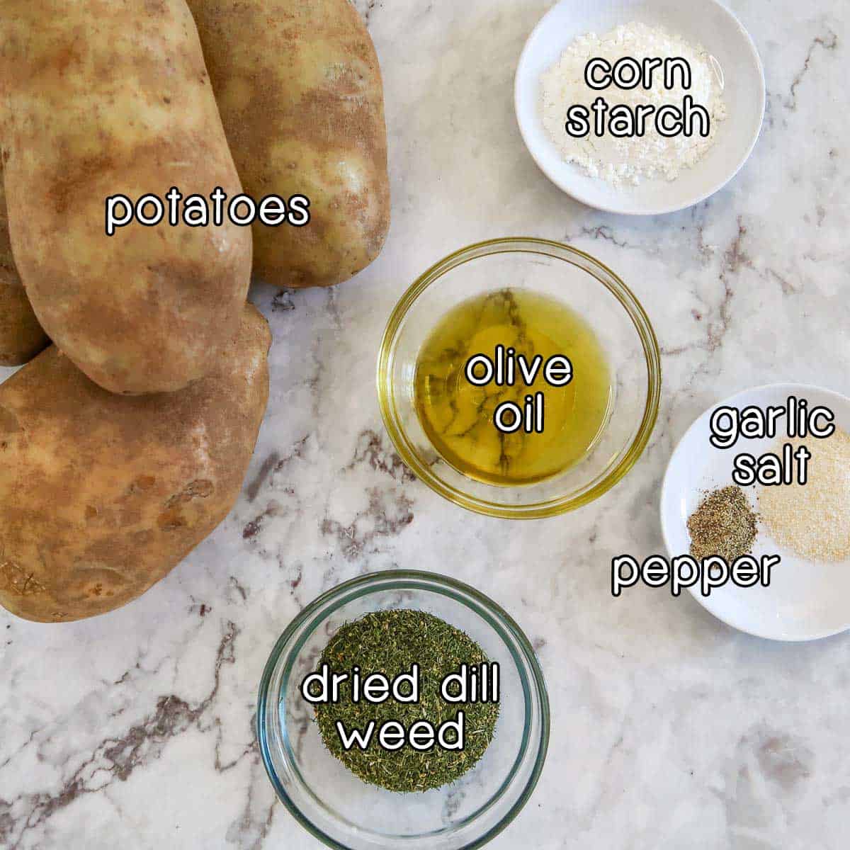 Overhead shot of ingredients - potatoes, corn starch, olive oil, dried dill weed, garlic salt, and pepper.