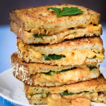 Close up side view of four halves of grilled cheese stacked on each other garnished with herbs on a white plate on a white surface.