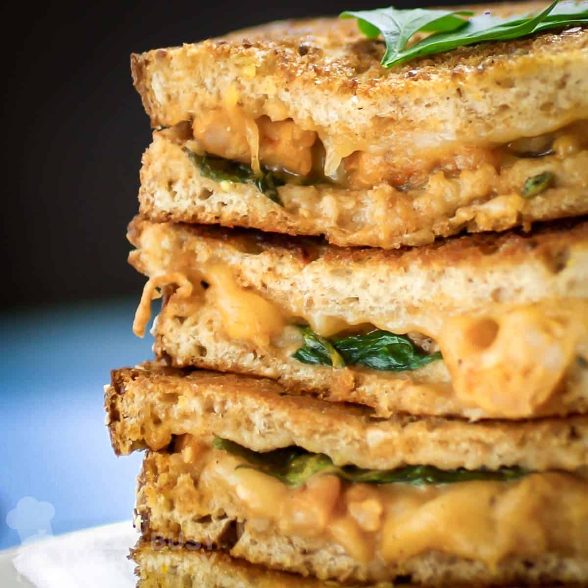 Close up side view of four halves of grilled cheese stacked on each other garnished with herbs on a white plate on a white surface.