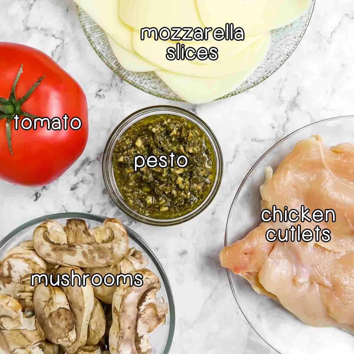 Overhead shot of ingredients- mozzarella slices, tomato, pesto, chicken cutlets, and mushrooms.