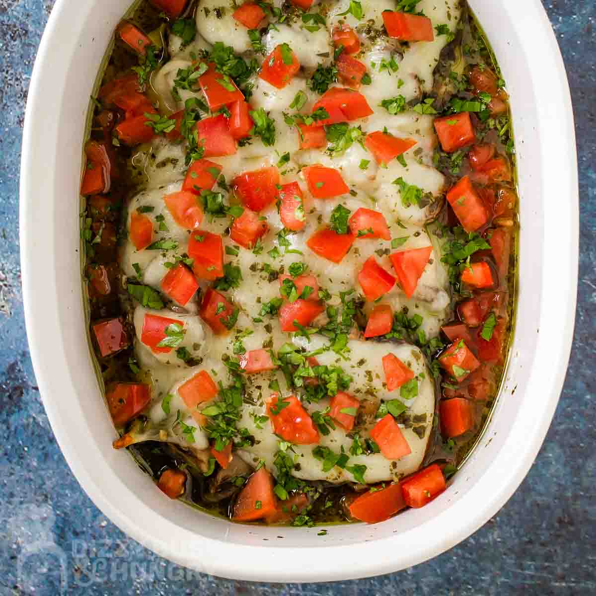 Overhead shot of pesto chicken in a deep white baking dish garnished with fresh tomato chunks and basil.