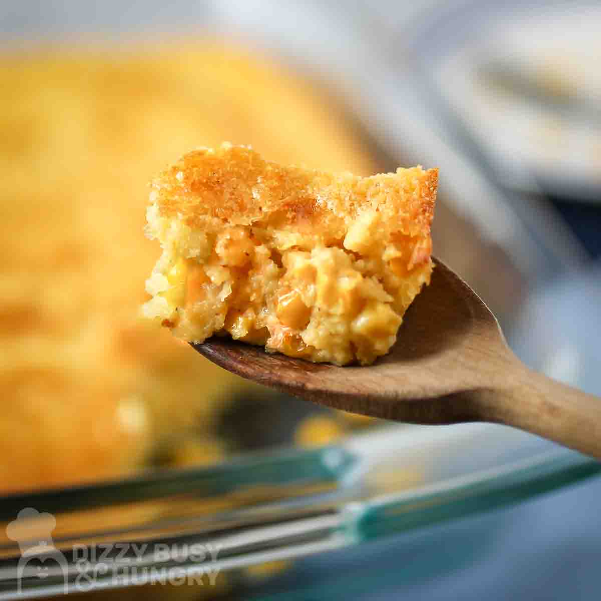 Close up view of a mouthful of corn casserole on a wooden spoon with the casserole dish in the backgroundClose up view of a mouthful of cornbread casserole on a wooden spoon with the casserole dish in the background