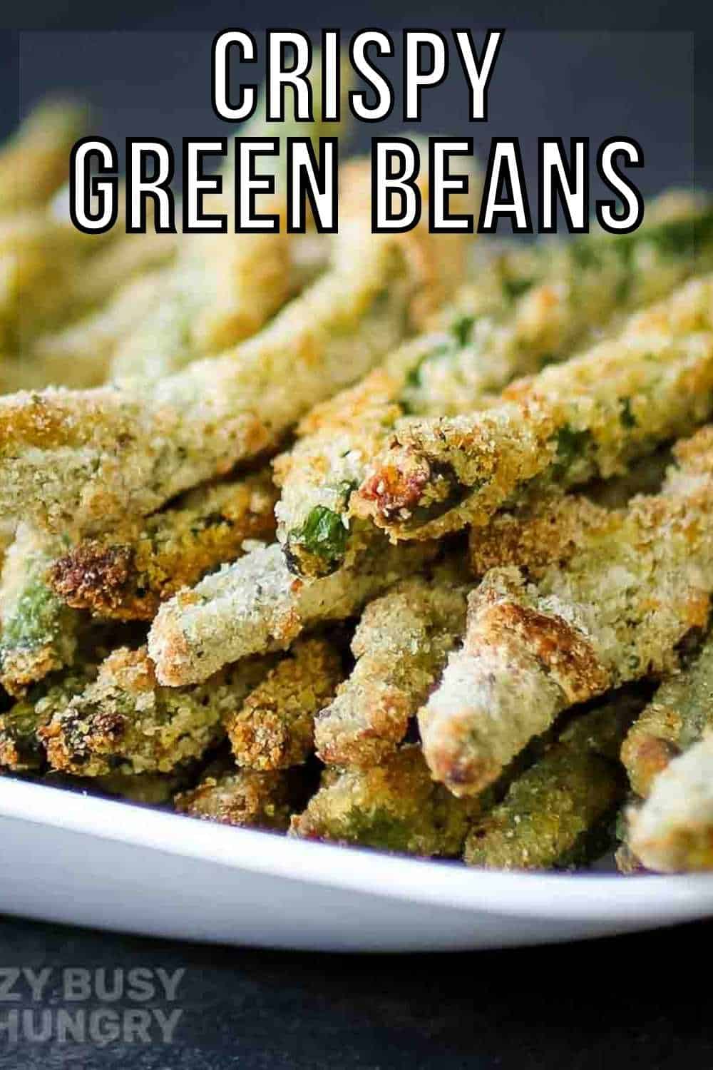 Side view of crispy baked green bean fries stacked on a white plate with a black background.