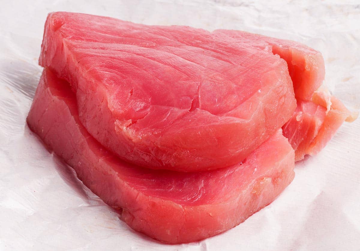 Two fresh fish steaks stacked on a piece of food wrapping paper.