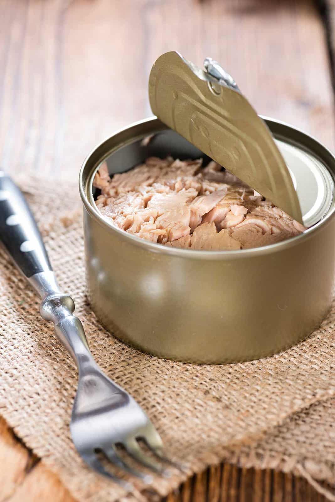 Open can of chunk light on burlap fabric with a fork in the foreground.