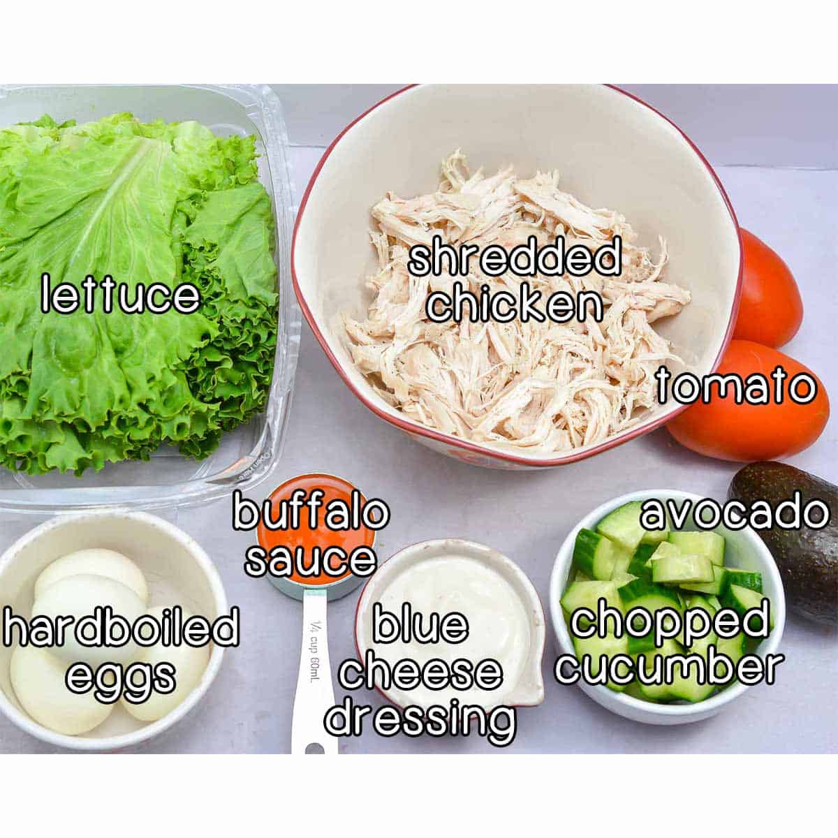 Overhead shot of ingredients- lettuce, shredded chicken, tomato, avocado, chopped cucumber, blue cheese dressing, buffalo sauce, and hardboiled eggs.
