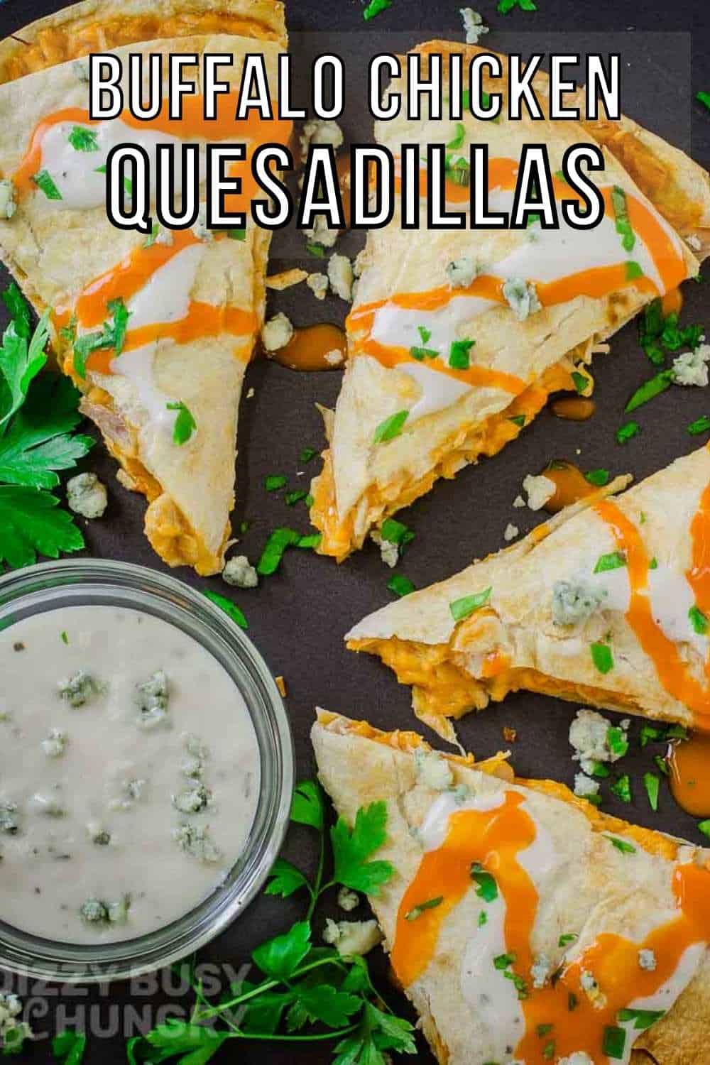 Overhead shot of a cut quesadilla drizzled with buffalo sauce and blue cheese garnished with herbs on a black plate with a side of ranch in a white bowl.