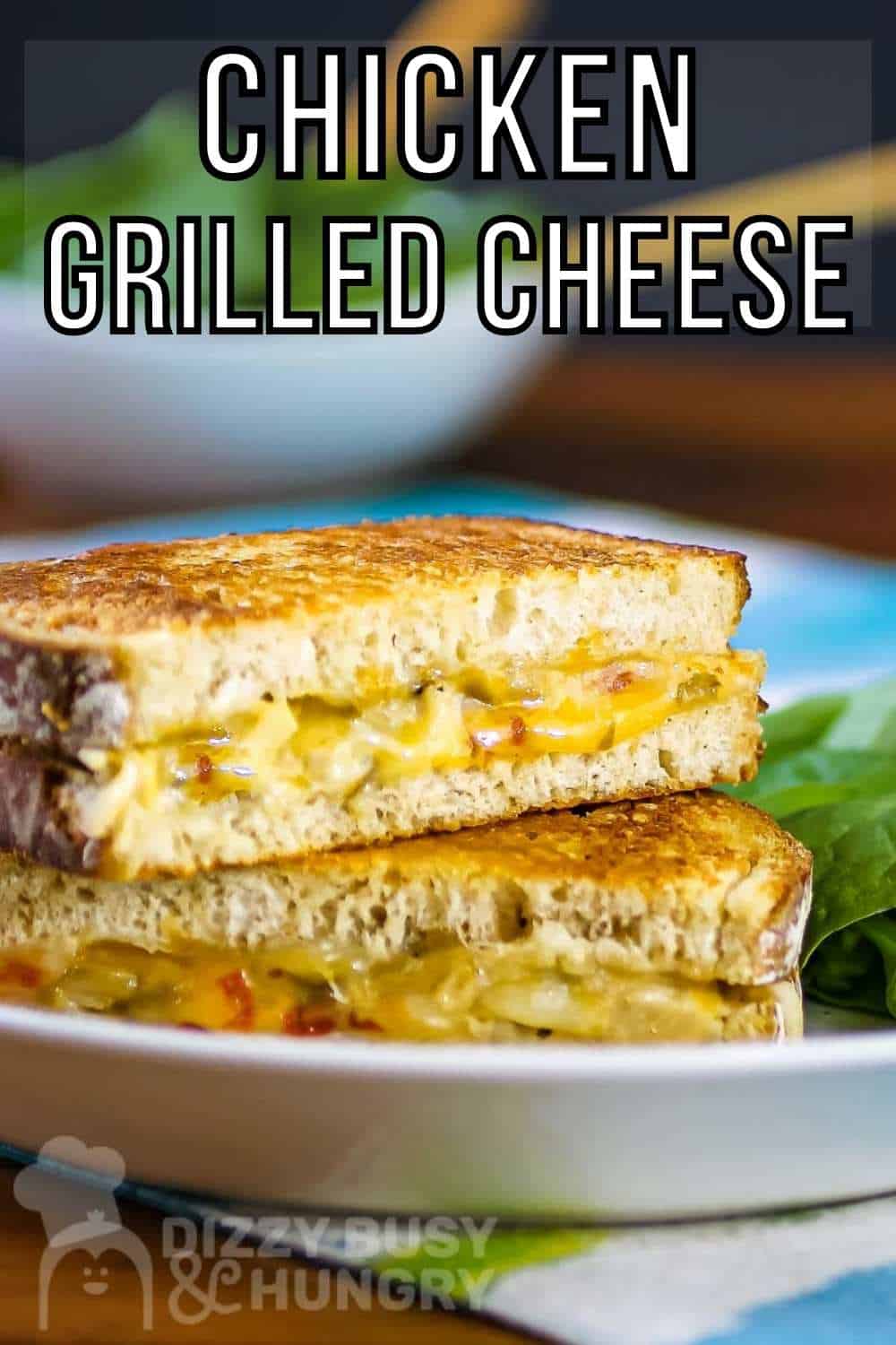 Side shot of two halves of grilled cheese sandwiches stacked on each other on a white plate with a side of greens on a blue and green cloth.