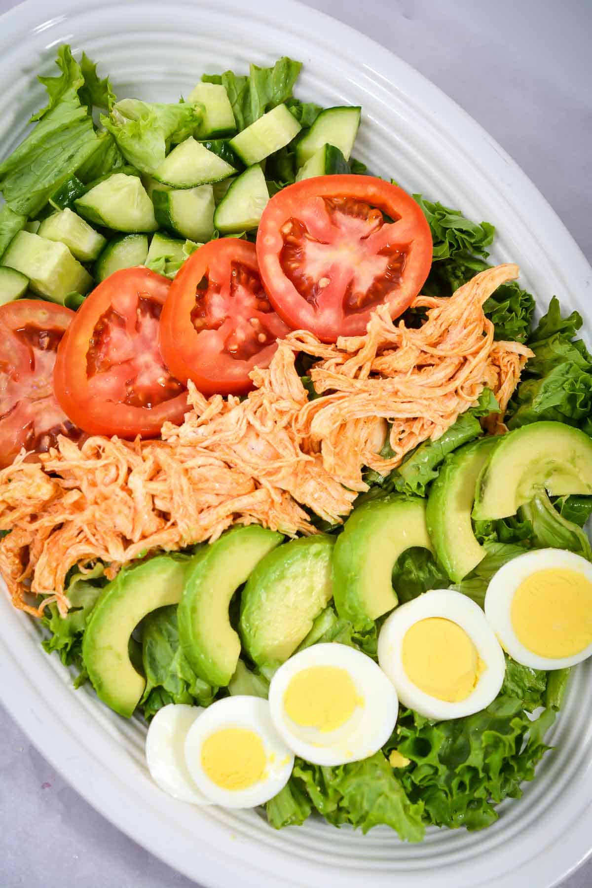 Overhead shot of the whole buffalo chicken salad with toppings arranged in lines in a large white oval dish.