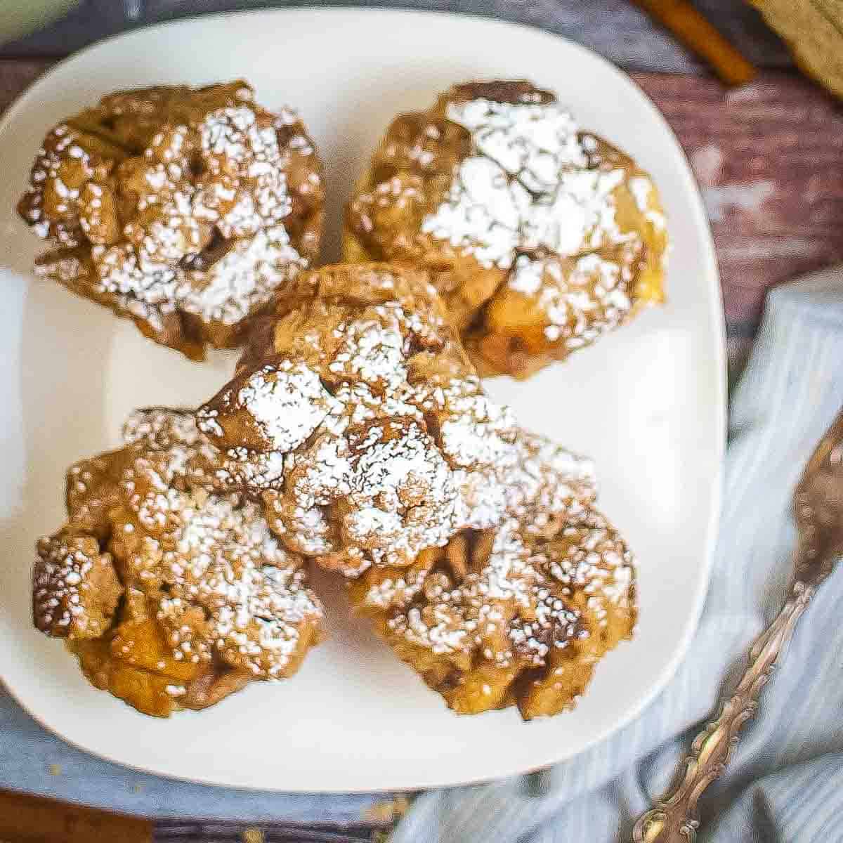 Overhead shot of five French toast cups garnished with powdered sugar arranged on a white square plate with a fork and blue cloth on the side.