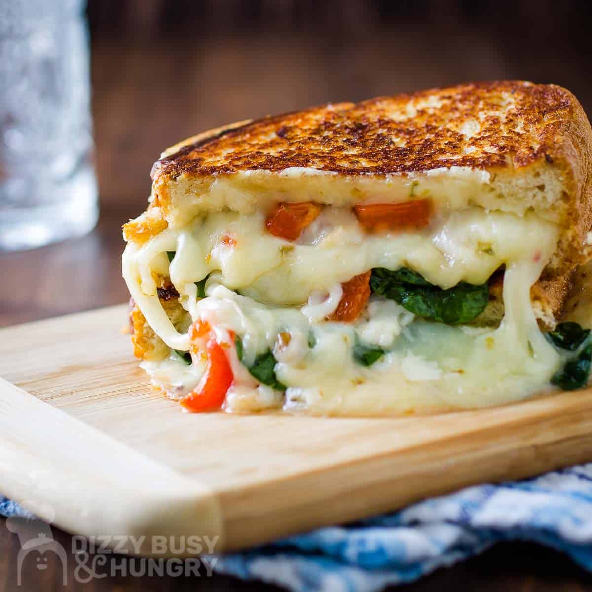 Side close up shot of a grilled cheese split in half with melty cheese down the side on a wooden cutting board on a blue plaid cloth.