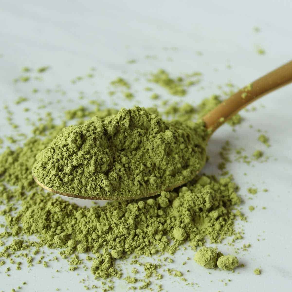 Green tea powder on a wooden spoon spilling over onto a white surface.