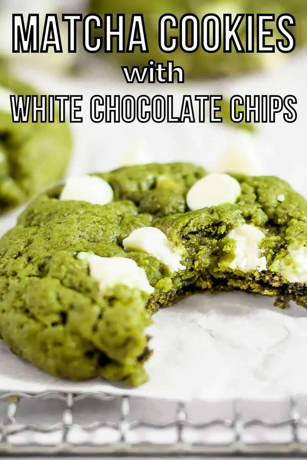 Side shot of a green matcha cookie with a bite taken out on a drying rack with parchment paper with more cookies and white chocolate in the background.