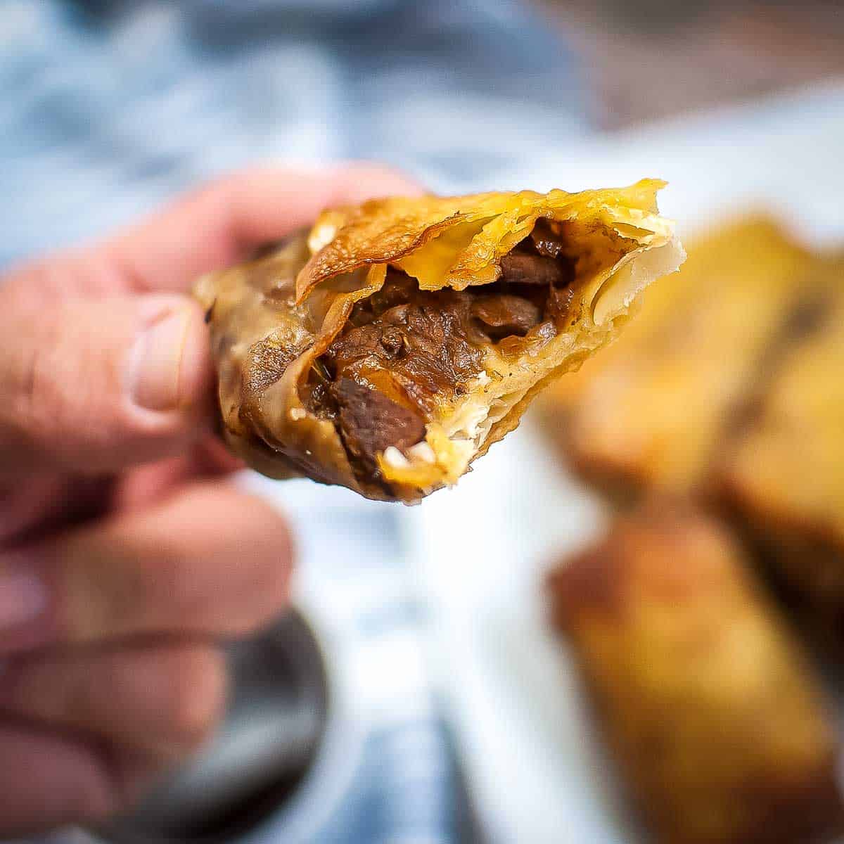 Close up shot of a hand showing the inside of an egg roll with more that are blurry in the background on a white plate.