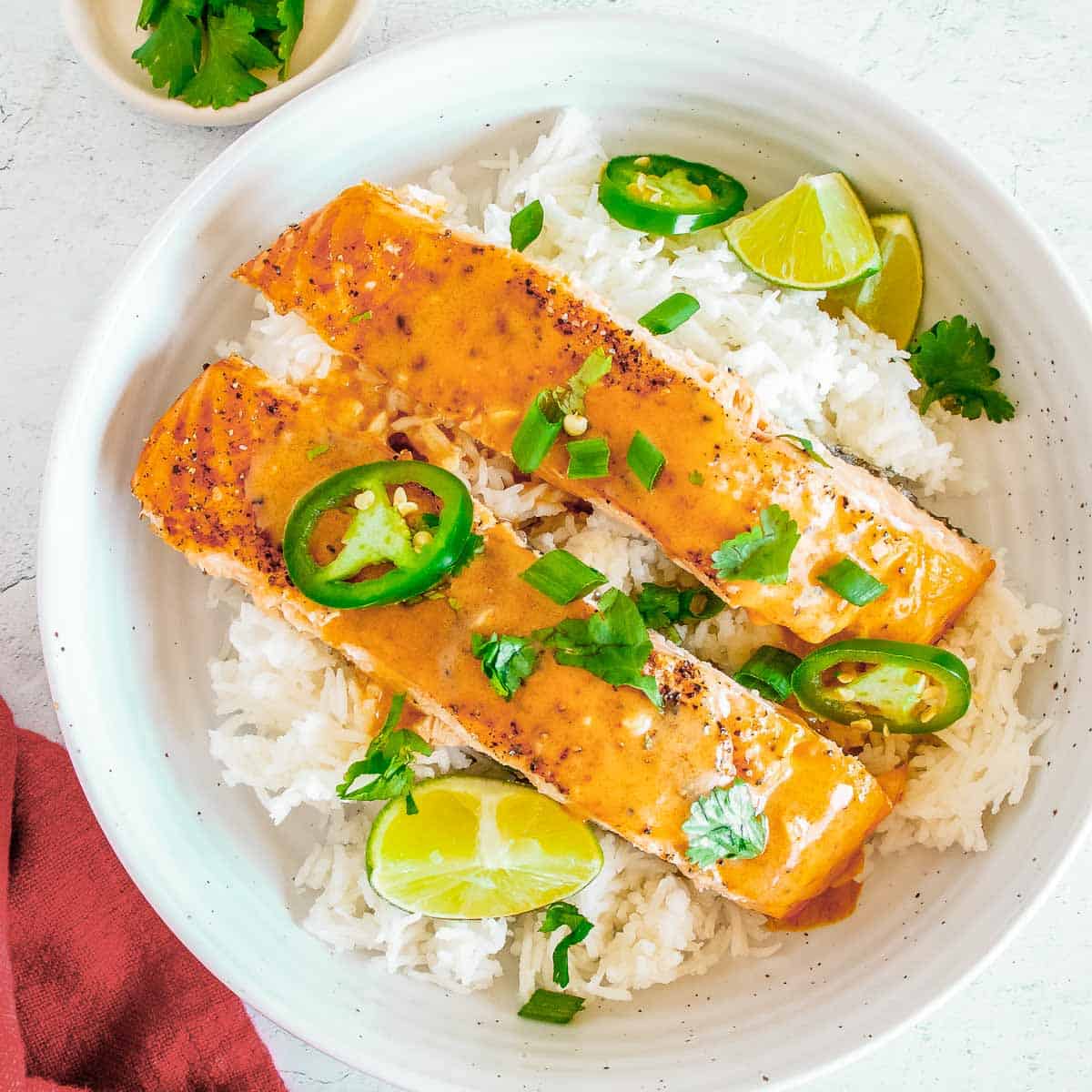 Overhead view of two pieces of salmon on a bed of rice garnished with parsley and cut jalapeños in a large white bowl with lime wedges on the side.