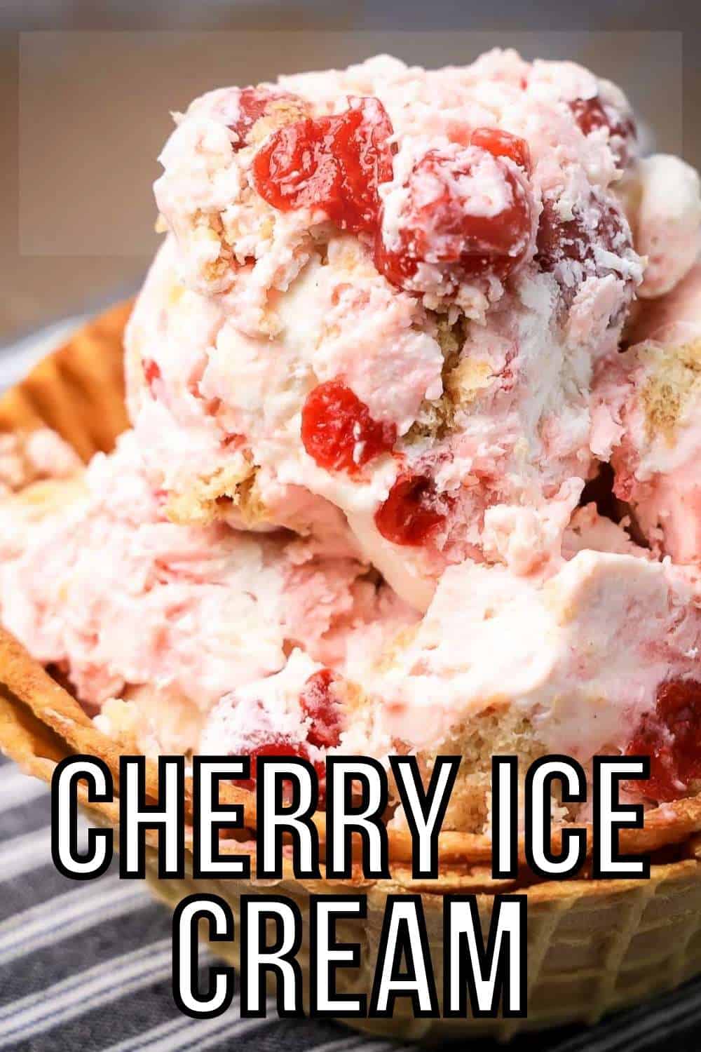 Side close up view of cherry vanilla ice cream in a waffle cone bowl on a black and white striped cloth.