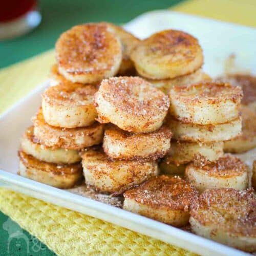 Pan fried banana snacks piled on a white square dish and placed on yellow and green napkins.