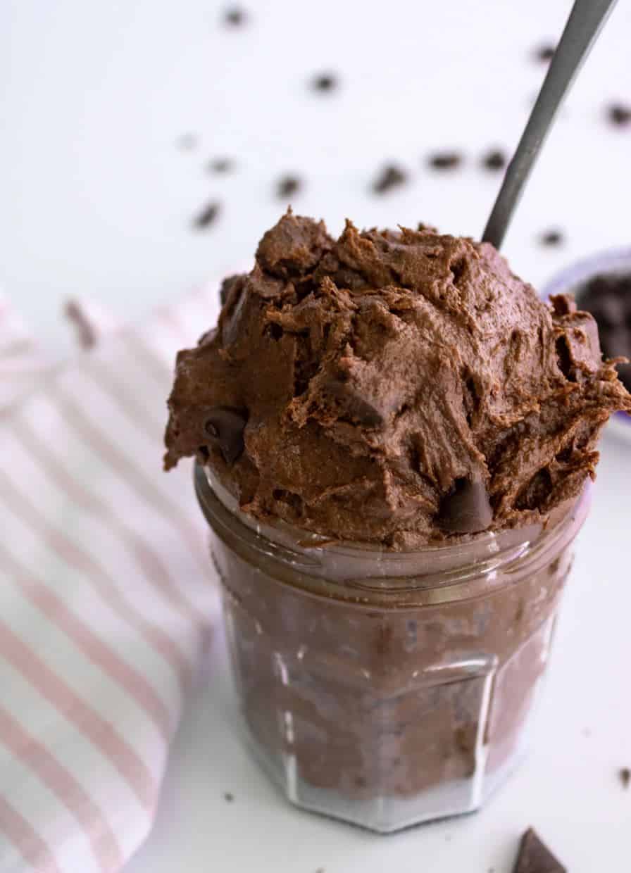 Brownie batter dip in a clear glass container with a spoon sticking out and garnished with chocolate chips.
