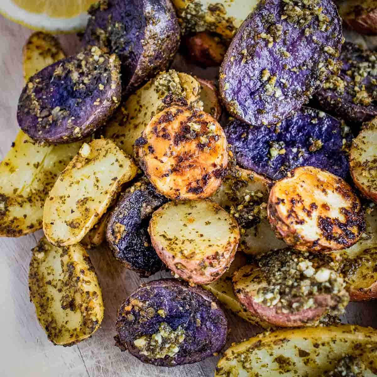 Close up shot of multicolor roasted pesto potatoes on a wooden surface.