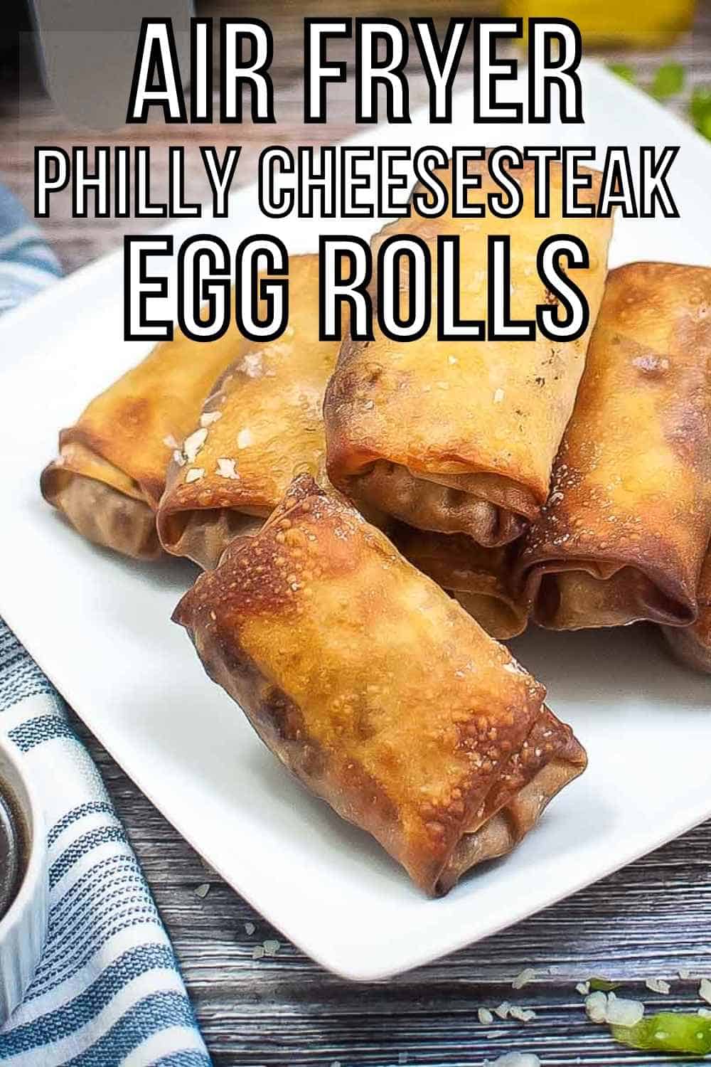 Side shot of multiple egg rolls arranged on a white square plate on a wooden surface with a blue striped cloth on the side.