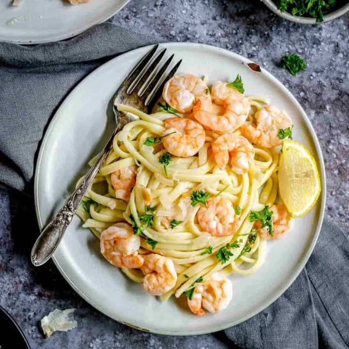 Overhead shot of shrimp scampi garnished with parsley on a grey plate with a fork on a black and grey surface.