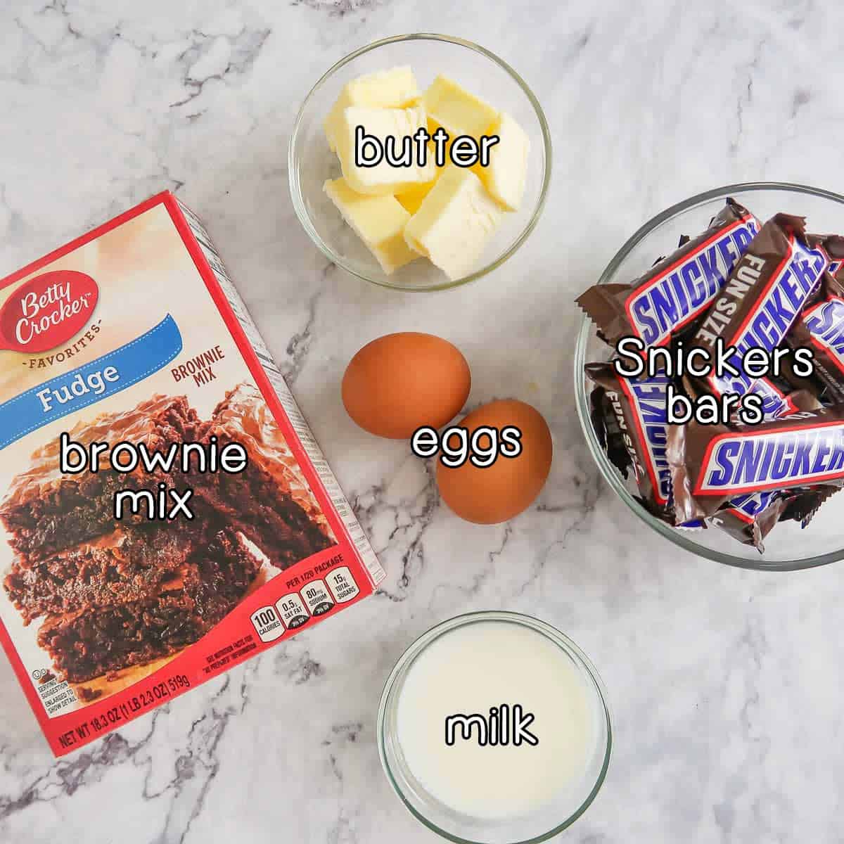 Overhead shot of ingredients - brownie mix, butter, eggs, milk, and snickers bars.