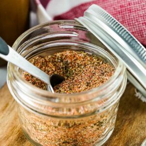 Side close up shot of steak rub in a glass jar with a tablespoon in it and the lid resting on the side.