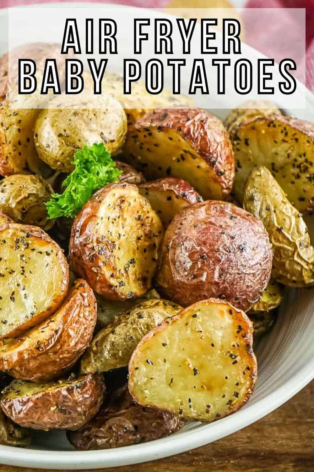 Side angled shot of halved baby potatoes garnished with fresh herbs in a white bowl on a wooden surface.