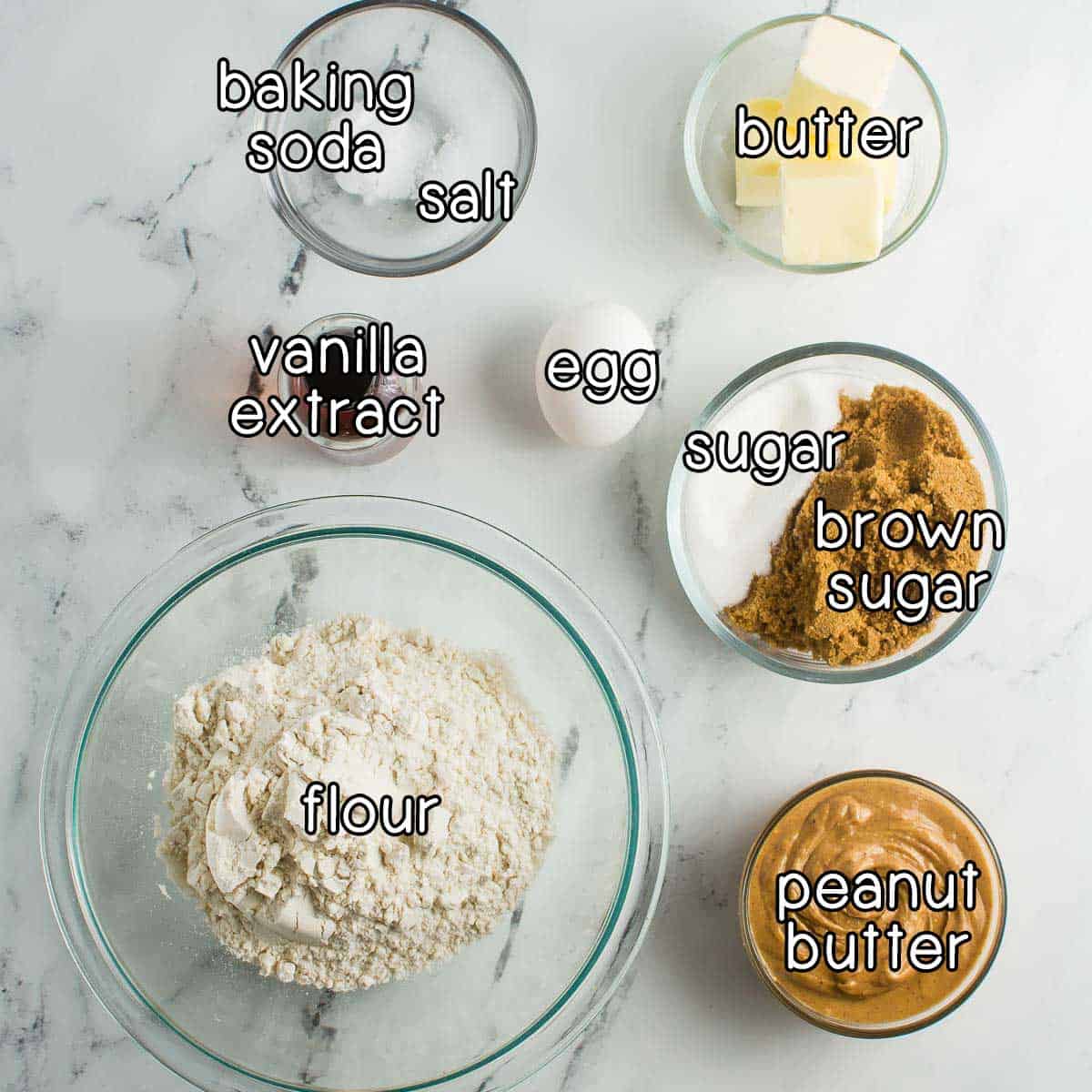 Overhead shot of ingredients - flour, vanilla extract, baking soda, salt, egg, butter, sugar, brown sugar, and peanut butter.