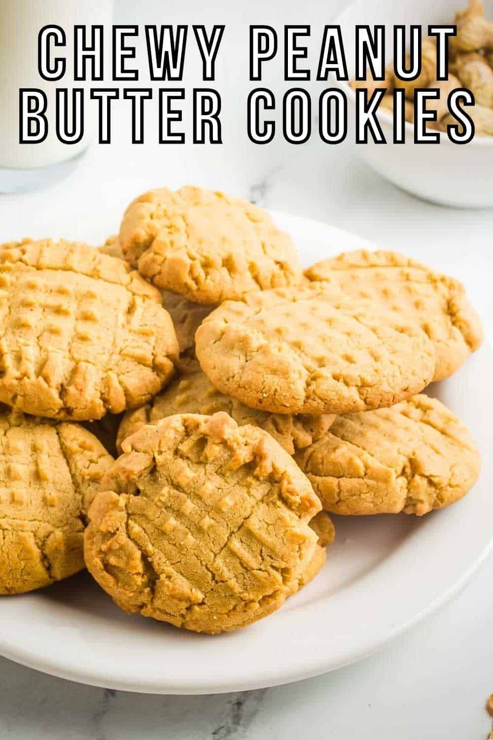 Side shot of multiple peanut butter cookies arranged on a white plate on a white marble surface.