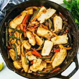 Overhead shot of chicken fajitas in a black skillet with fresh herbs on the side.