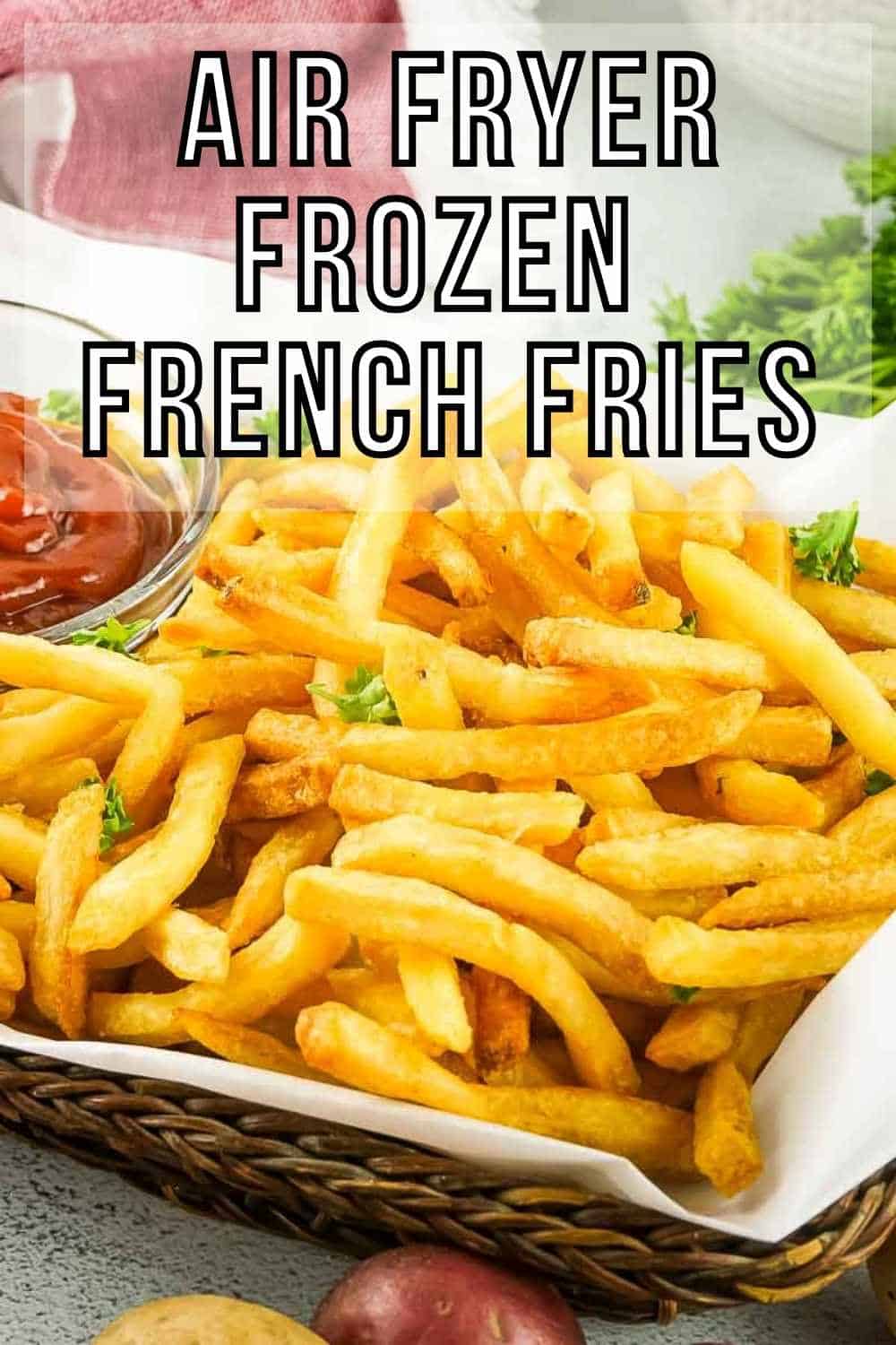 Side shot of French fries garnished with herbs in a basket lined with parchment paper and ketchup on the side in a clear bowl.