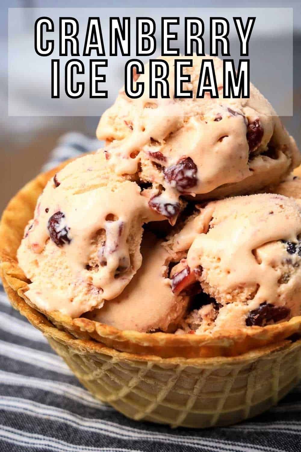 Side close up shot of multiple scoops of ice cream with cranberries in a double layered waffle cup sitting on a black and white striped cloth.