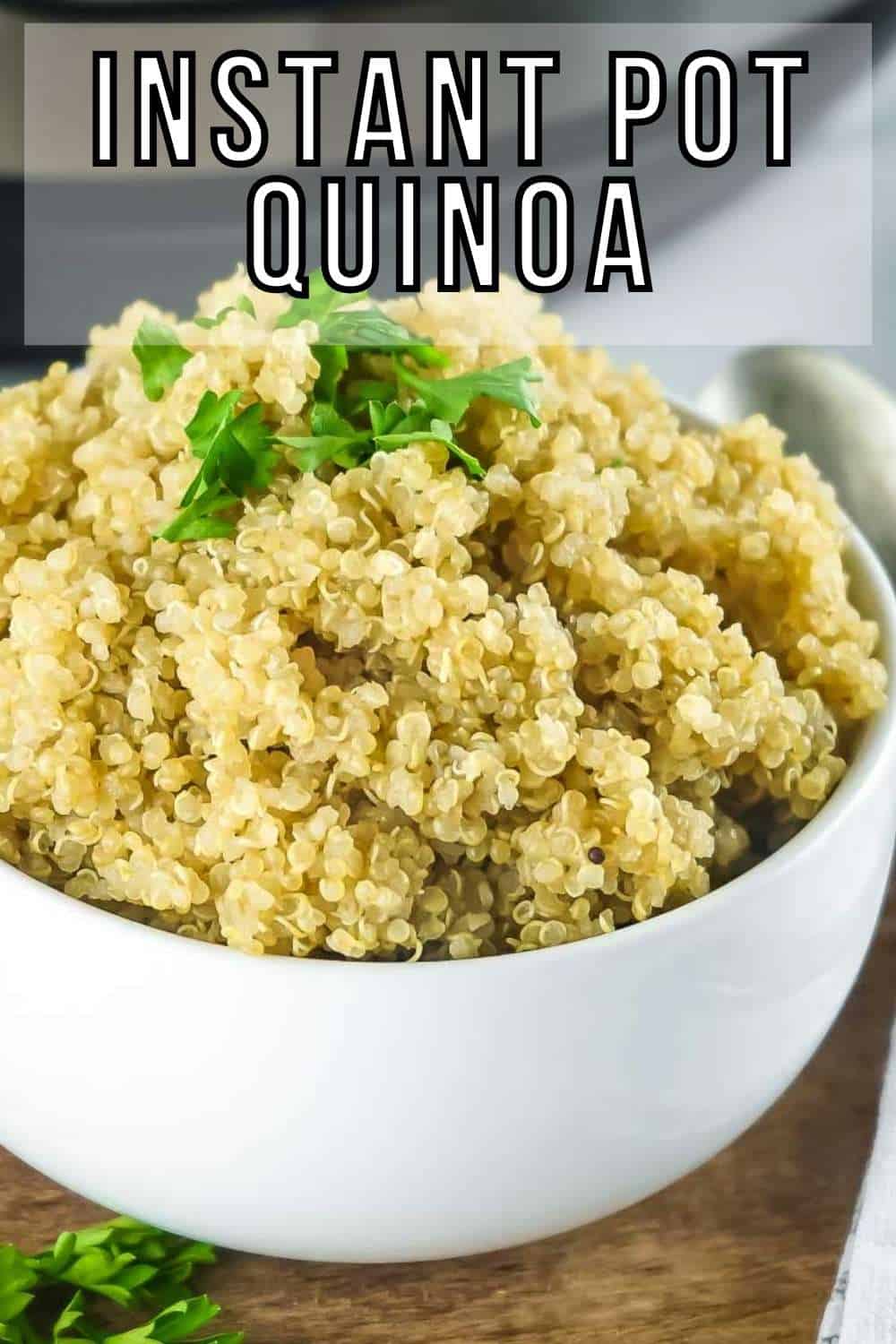 Side shot of a white bowl of fluffy quinoa garnished with fresh herbs on a wooden surface.