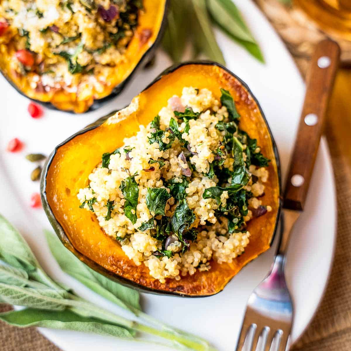 Overhead shot of two halves of an acorn squash filled with quinoa filling on a white oval plate with sage and a wooden fork on the side.