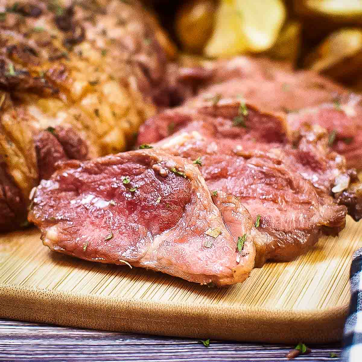 Side close up shot of a full lamb roast with slices of lamb and potato wedges on the side on a wooden cutting board.