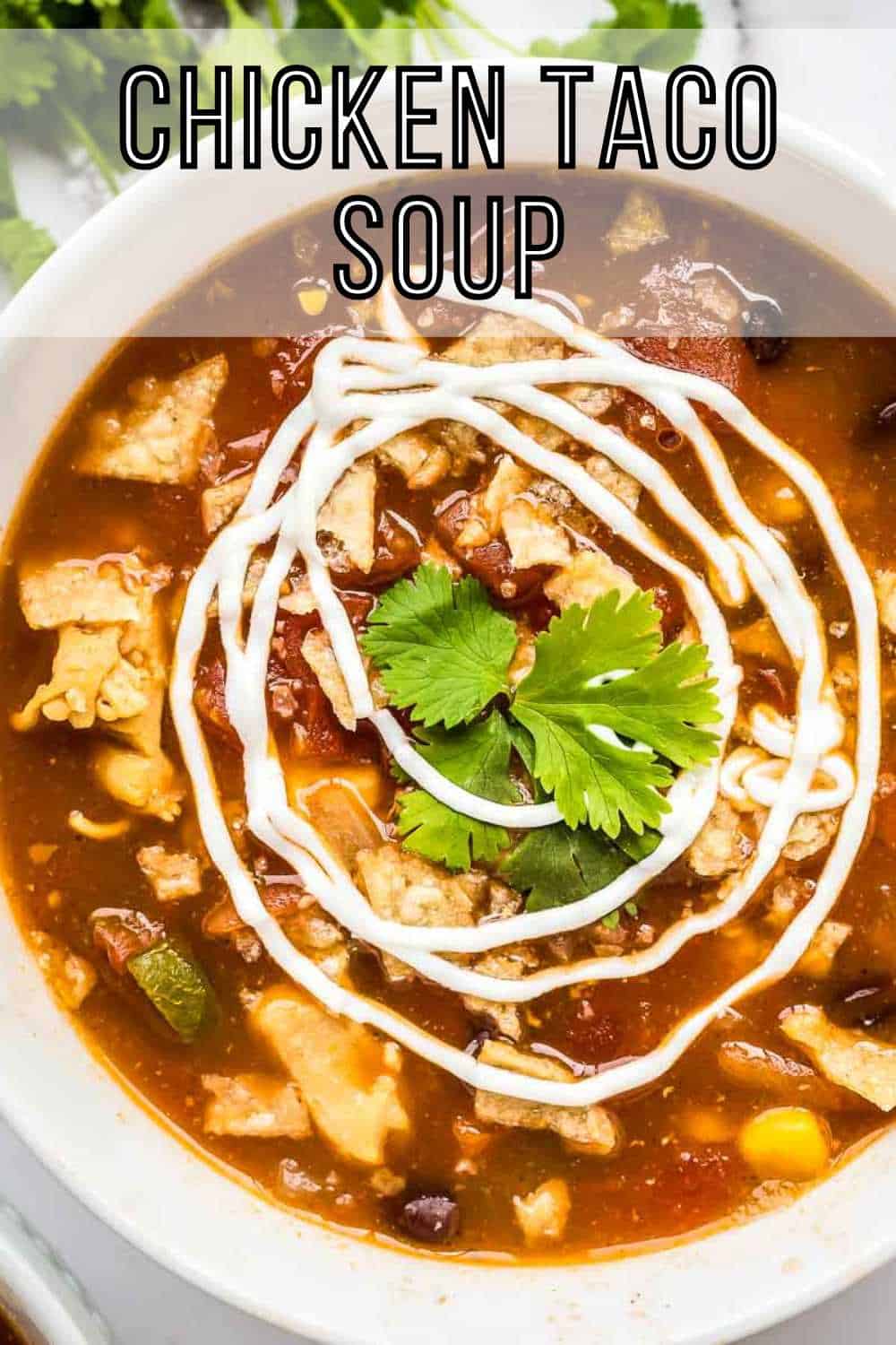 Overhead shot of chicken tortilla soup in a white bowl garnished with swirls of sour cream and fresh herbs.