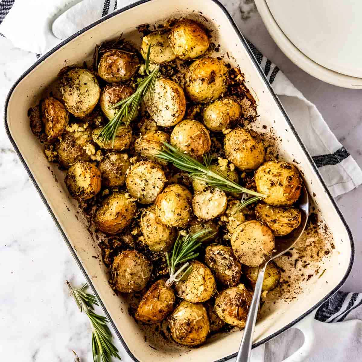 Overhead shot of a white rectangle pan with rosemary potatoes garnished with fresh rosemary with a spoon on the side.