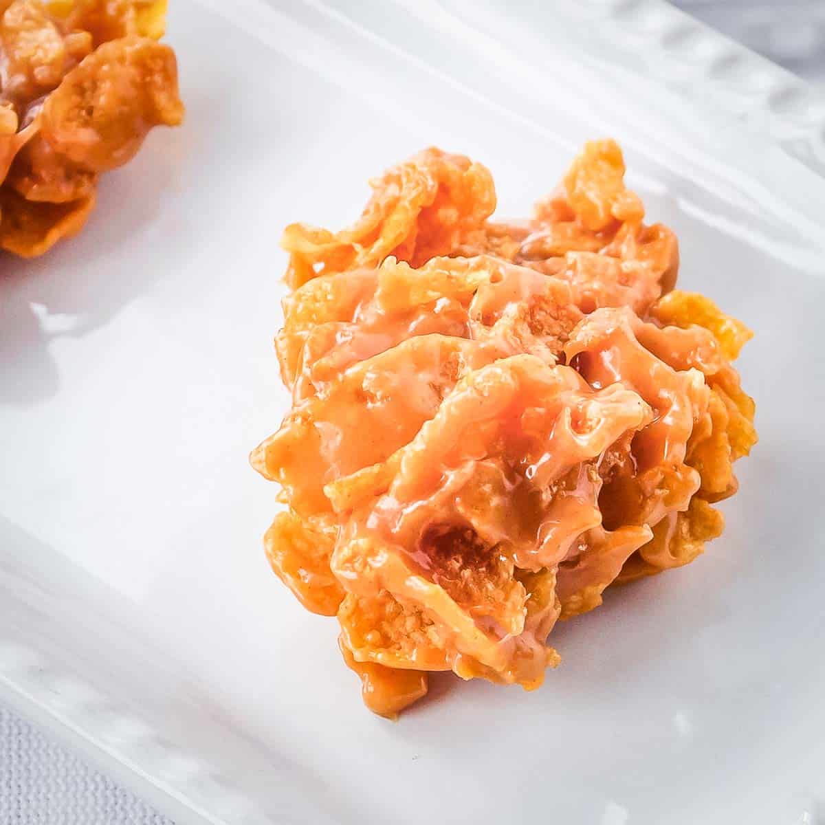 Side close up shot of a cornflake cookie on a white plate.