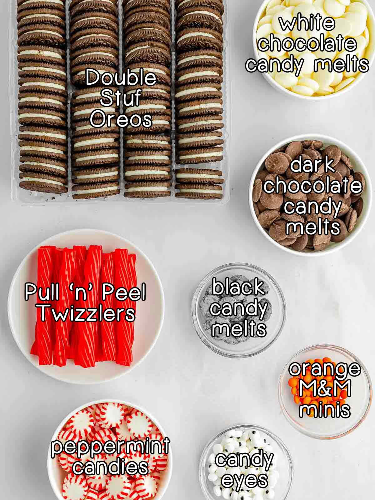 Overhead shot of ingredients - double stuffed Oreos, white chocolate candy melts, dark chocolate candy melts, black candy melts, pull n peel twizzlers, peppermint candies, candy eyes, and orange M&M minis.