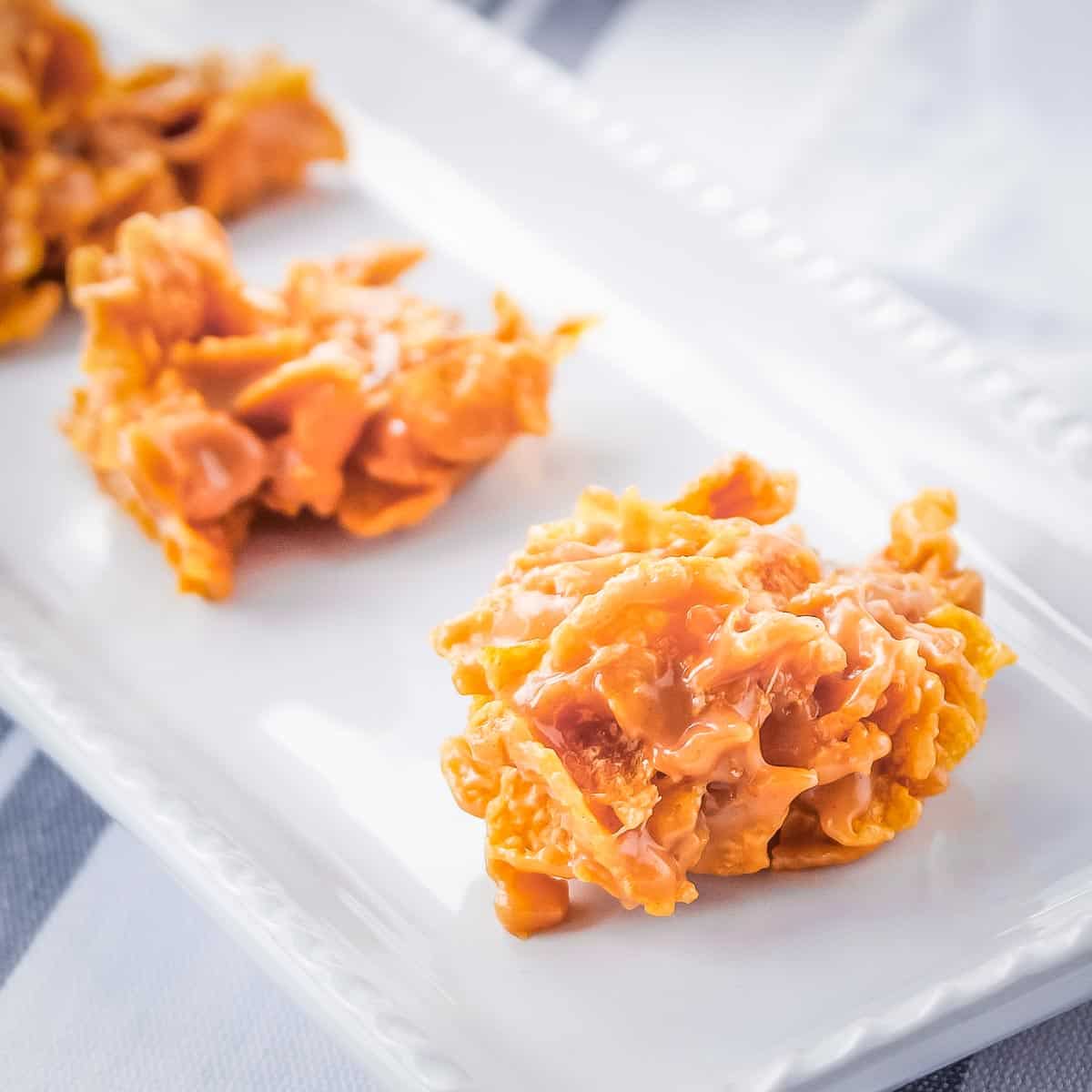 Side angled shot of multiple cornflake cookies on a white plate.