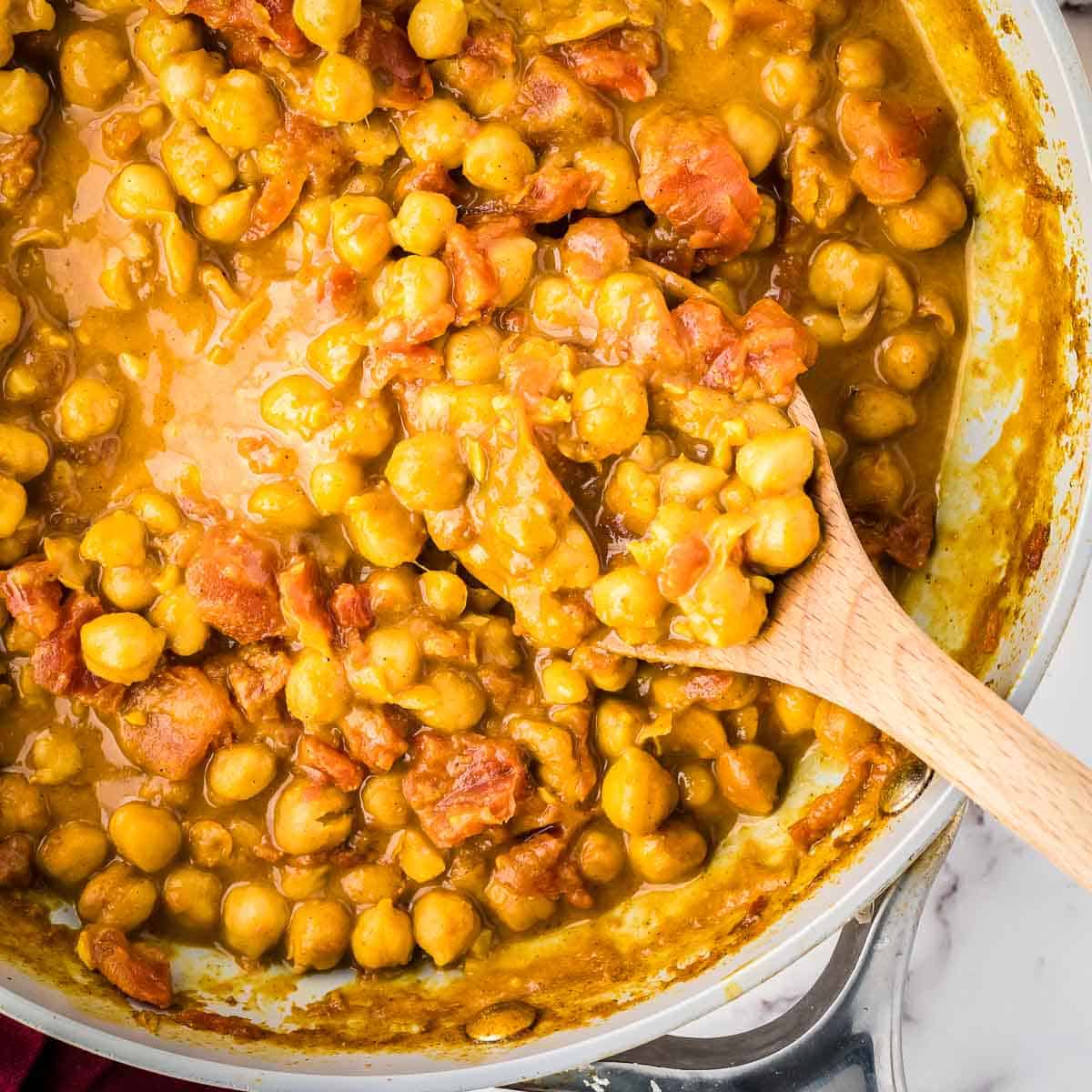 Overhead shot of chickpea curry in a skillet with a wooden spoon taking a spoonful out.