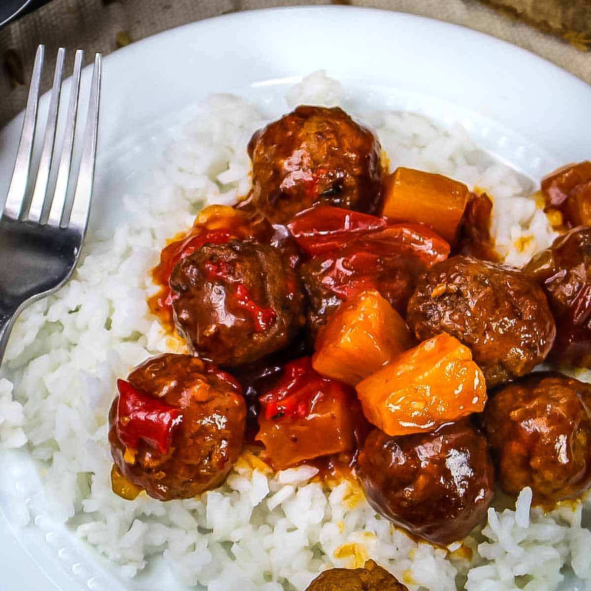 Overhead close up shot of Hawaiian meatballs over white rice in a white bowl with a fork on the side of the bowl.