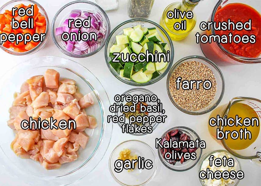 Overhead shot of ingredients - red bell peppers, red onions, zucchini, olive oil, crushed tomatoes, farro, chicken broth, feta cheese, kalamata olives, garlic, oregano, dried basil, red pepper flakes, and chicken.