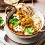 Overhead close up shot of tikka masala with rice in a brown speckled bowl on a grey plate garnished with yogurt and parsley.