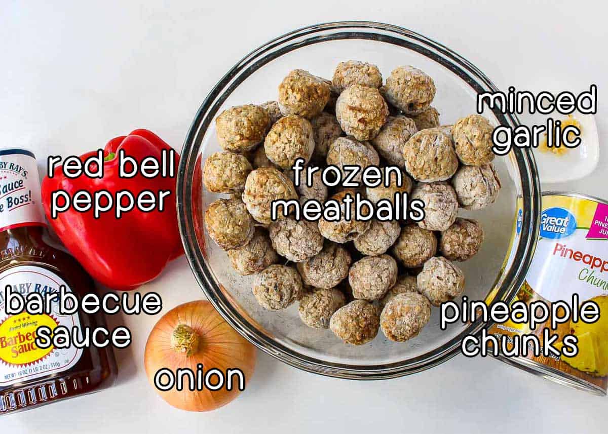 Overhead shot of ingredients - minced garlic, pineapple chunks, frozen meatballs, red bell pepper, onion, and barbecue sauce.