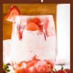 Side shot of a glass tumbler with strawberry mousse and sliced strawberries on a. marble table with gold spoons and strawberries on the side.